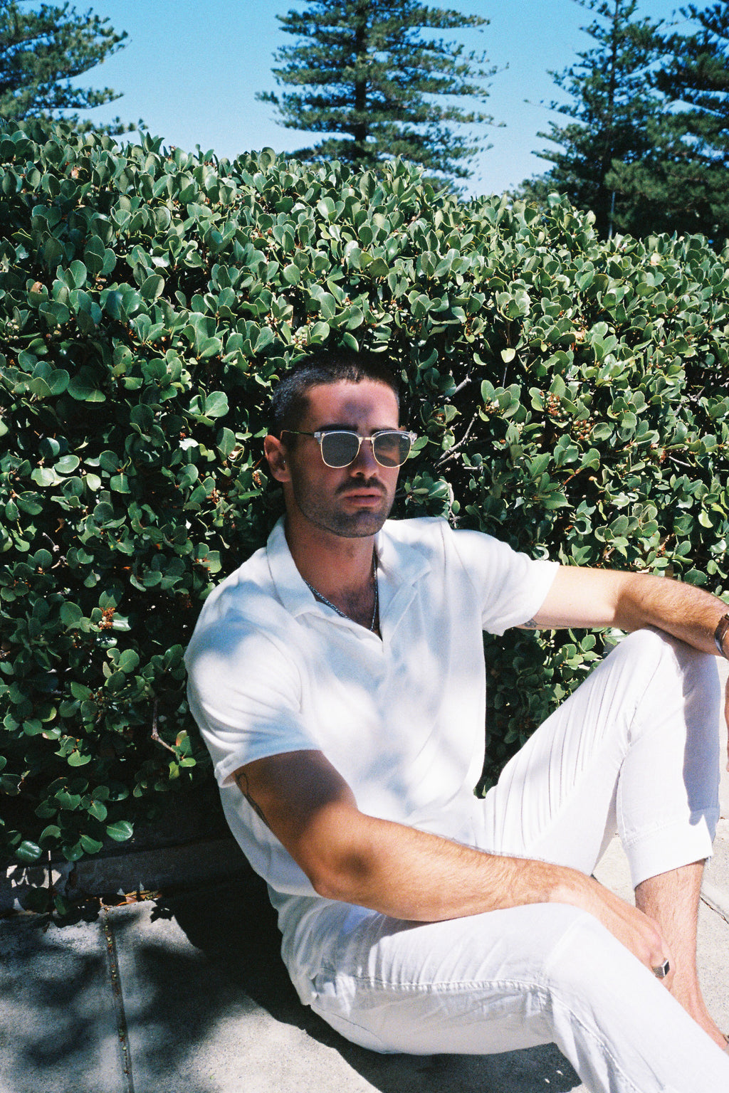 Terry towelling polo shirt in white, worn by a man reclining against a green setting