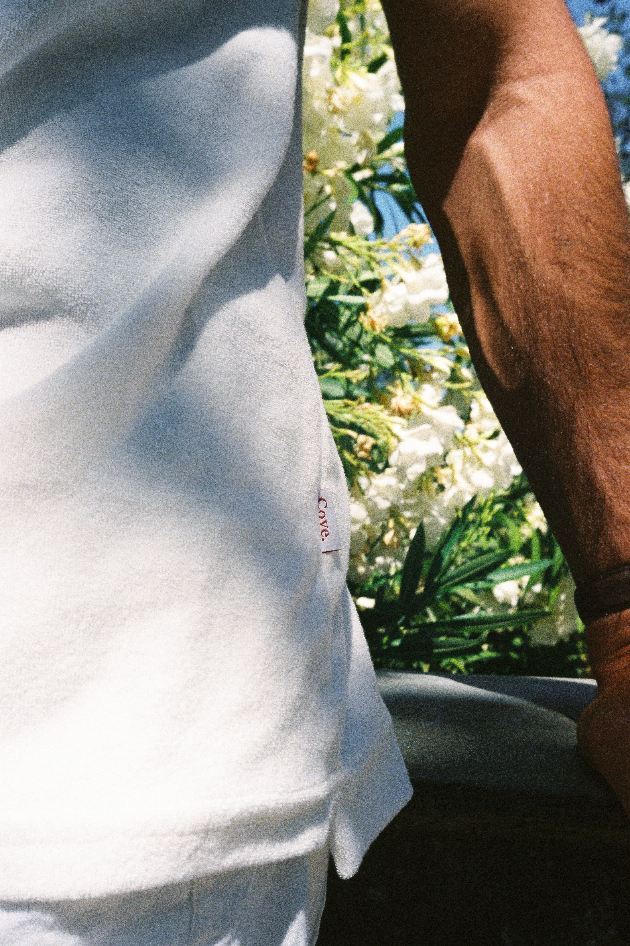 Close shot of the terry towelling polo shirt in white, with the Cove side tag shown