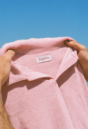 Terry towelling polo shirt in salmon pink held against the sky